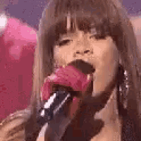 a close up of a woman singing into a microphone with her mouth open .