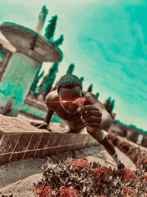 a man is holding a flower in front of his face with a fountain in the background