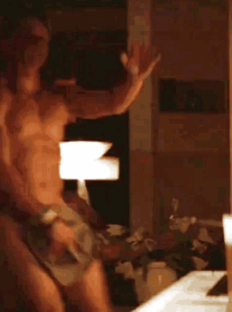a shirtless man is dancing in front of a mirror in a dark room .