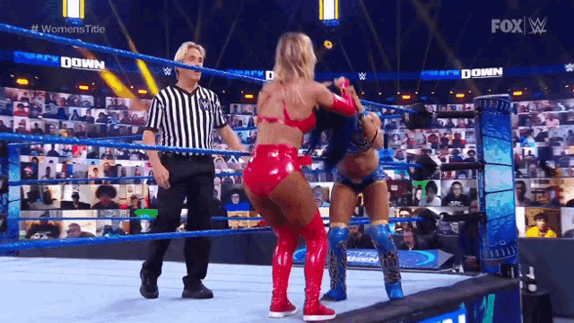 two women are wrestling in a wrestling ring while a referee stands behind them .
