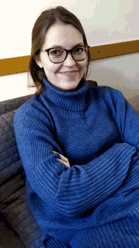 a woman wearing glasses and a blue sweater sits on a couch