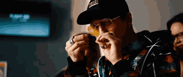 a man wearing a hat , sunglasses and a ring is holding something in his hand .