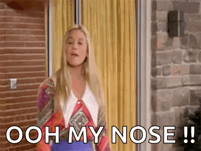 a woman is standing in front of a yellow curtain and saying ooh my nose .