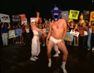 a man in underwear is dancing in front of a crowd holding signs including one that says " blink 182 "