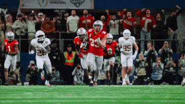a group of football players are running on a field and one has the number 85 on his shorts