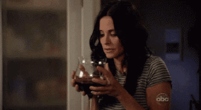 a woman in a striped shirt is holding a glass of wine with the abc logo on her arm