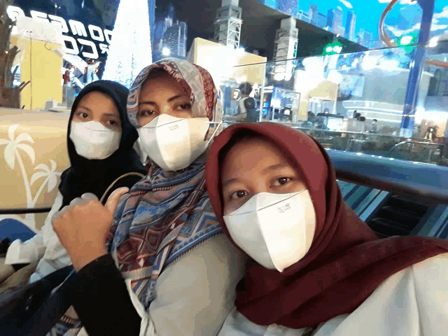 three women wearing face masks with one wearing a scarf that says ' hijab ' on it