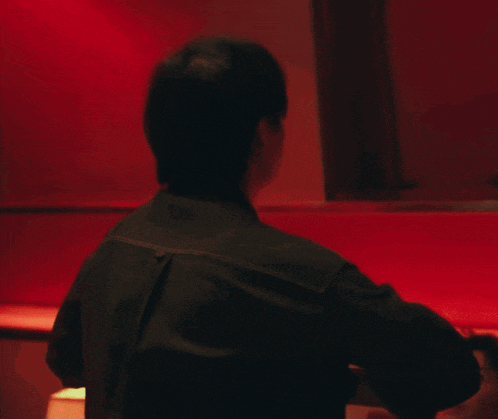 a man with a tattoo on his back is sitting in front of a red wall
