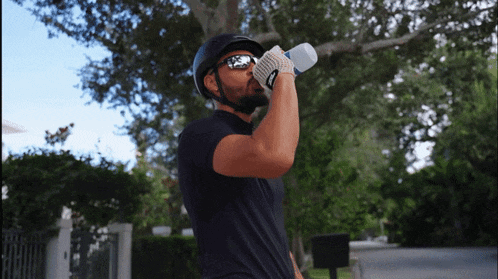 a man wearing a helmet and sunglasses drinks from a water bottle