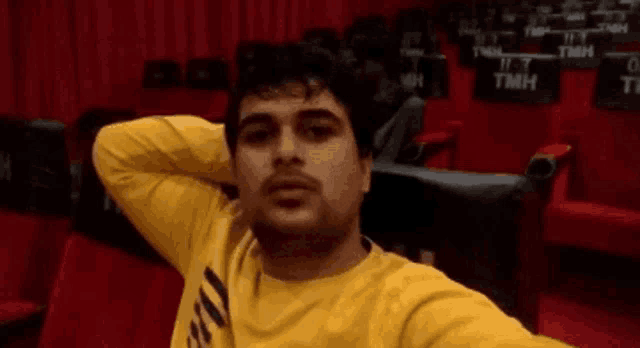 a man in a yellow shirt is taking a selfie in an auditorium