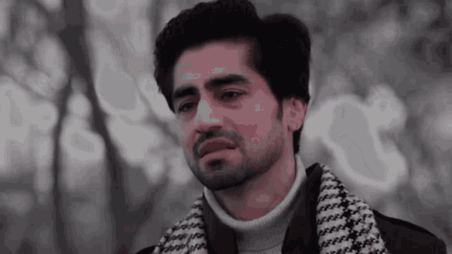 a man wearing a turtleneck sweater and a scarf is crying in a park .