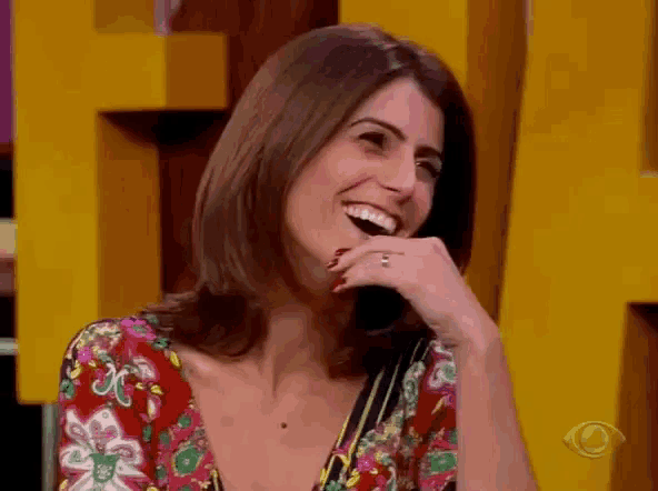 a woman in a floral shirt is laughing with her hand on her face