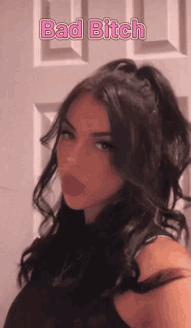 a girl with black hair is standing in front of a door with the words bad bitch written on it