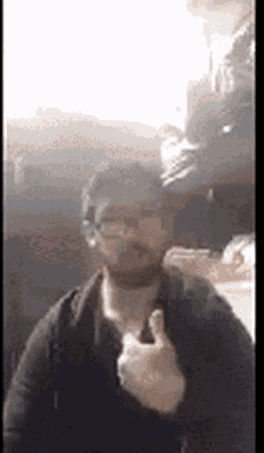 a man with glasses and a hat is giving a thumbs up .