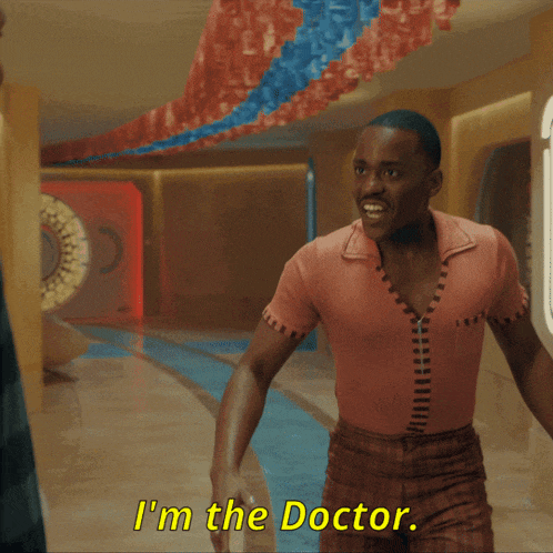 a man in a pink shirt is talking to another man and says " i 'm the doctor "