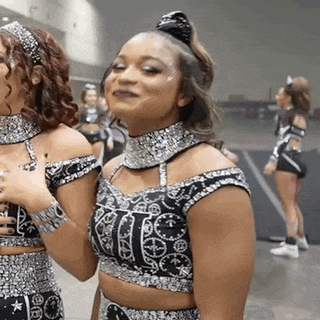 two cheerleaders are standing next to each other and one of them is wearing a black and silver outfit .