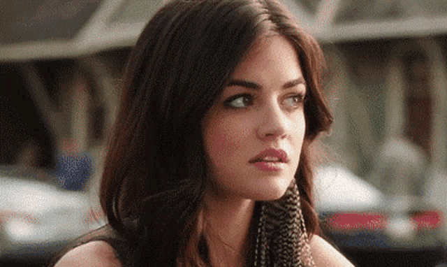 a woman with long dark hair and a scarf around her neck is looking at the camera .