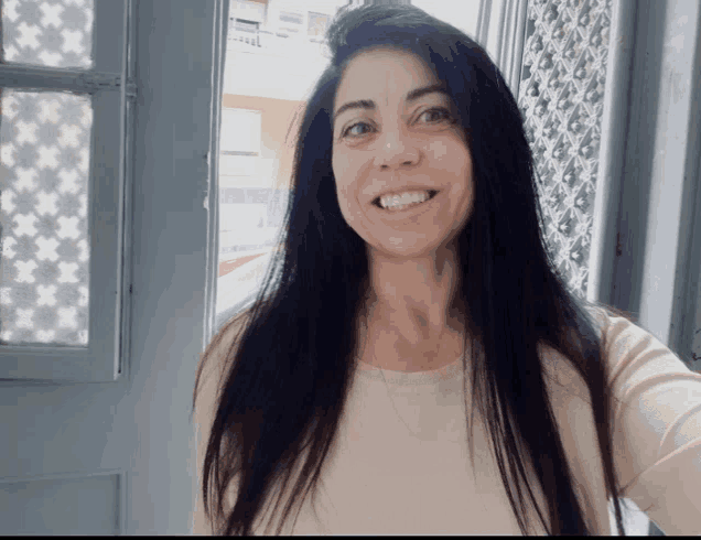 a woman with long black hair smiles in front of a window