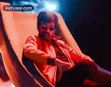 a man with a mustache and sunglasses is sitting in a chair with his legs crossed .