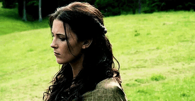 a woman is standing in a grassy field with her head down .