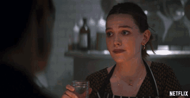 a woman is holding a glass of water and a netflix logo can be seen behind her