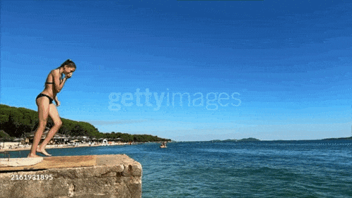 a girl in a bikini is jumping into the ocean from a pier