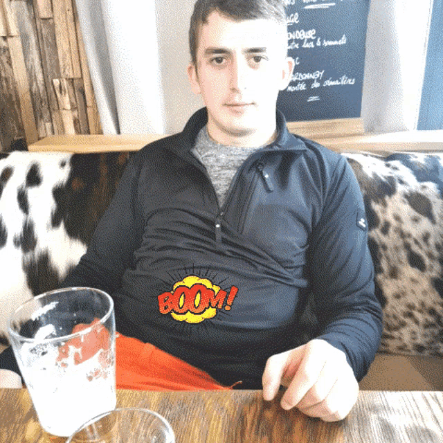a man wearing a black shirt that says boom on it sits at a table