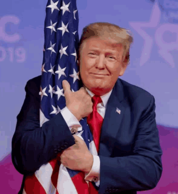 a man in a suit and tie is holding an american flag and smiling