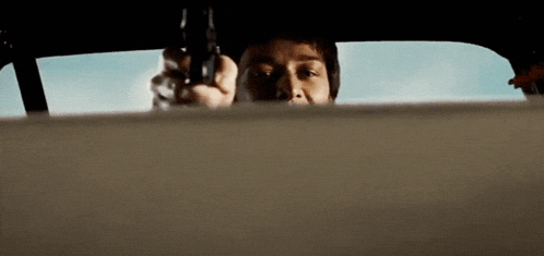 a man is pointing a gun at the camera while driving a car .
