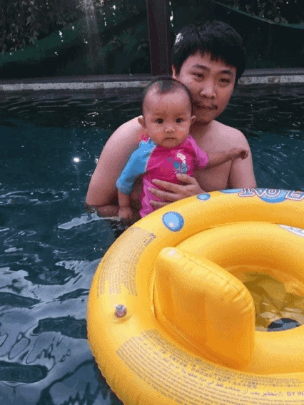 a man is holding a baby in a pool next to a float