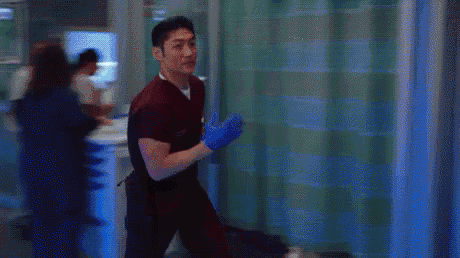 a man in a scrub top and blue gloves is standing in a room .