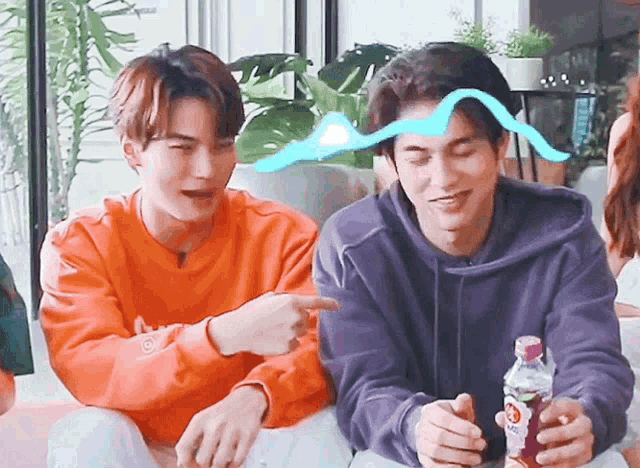 two young men are sitting on a couch and one is pointing
