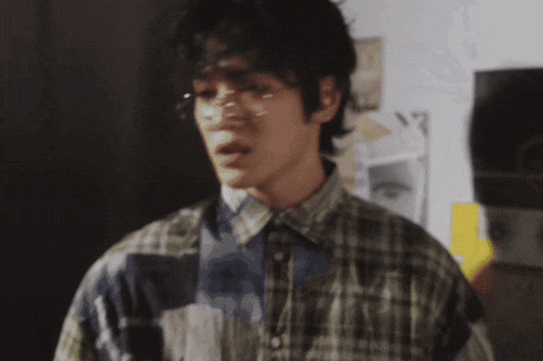 a man wearing glasses and a plaid shirt is standing in front of a bulletin board