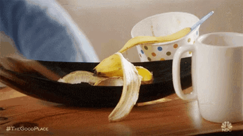 a person is peeling a banana in a bowl on a table next to a cup and spoon .