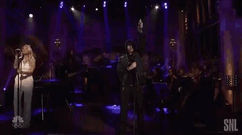 a man and a woman singing on a stage with the snl logo in the corner