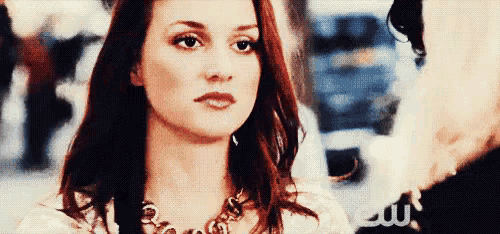 a woman with red hair is wearing a necklace and looking at someone .