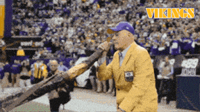 a man in a yellow jacket and a blue hat stands in front of a vikings sign