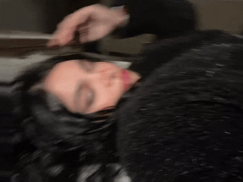 a blurry picture of a woman laying on her back with her eyes closed and a person holding her hair .