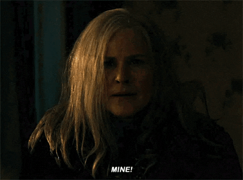a woman with long white hair is talking to someone in a dark room and saying mine .