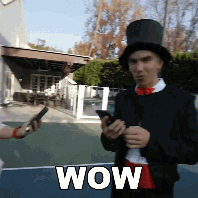 a man in a top hat is holding a cell phone and the word wow is on the bottom