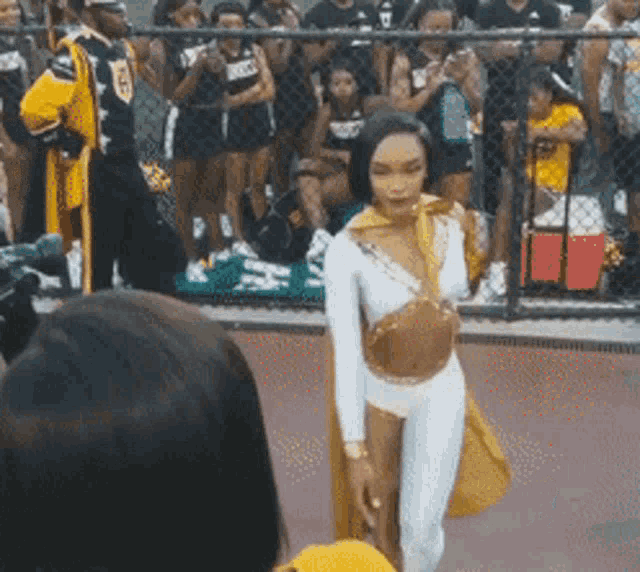 a woman in a yellow and white outfit is walking in front of a crowd