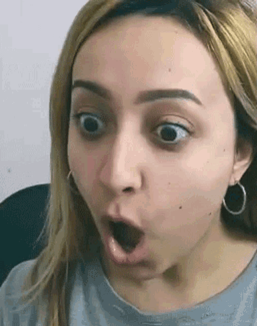 a woman with a surprised look on her face is wearing earrings and a gray shirt .