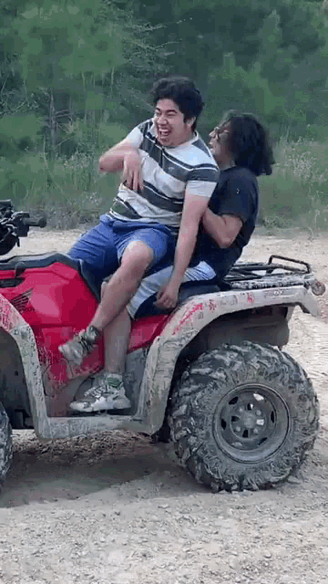 a man is riding on the back of another man on an atv in the dirt .