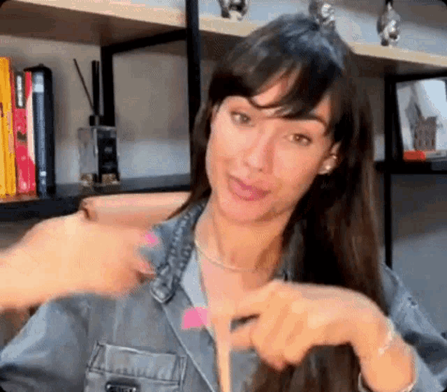 a woman in a denim jacket is sitting in front of a shelf with books .