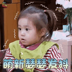 a little girl is sitting in front of a vase of flowers and making a surprised face .