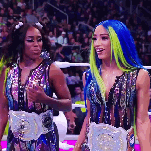 two women with blue and green hair are standing next to each other wearing championship belts