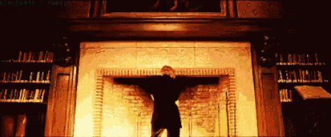 a man stands in front of a fireplace with his arms outstretched in a dark room