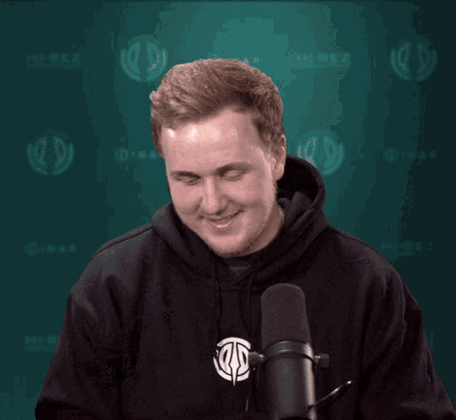 a man in a black hoodie is laughing in front of a microphone with the word hirez behind him