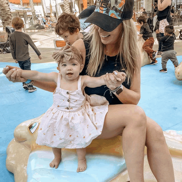 a woman is holding a baby while wearing a hat that says ' abercrombie & fitch '