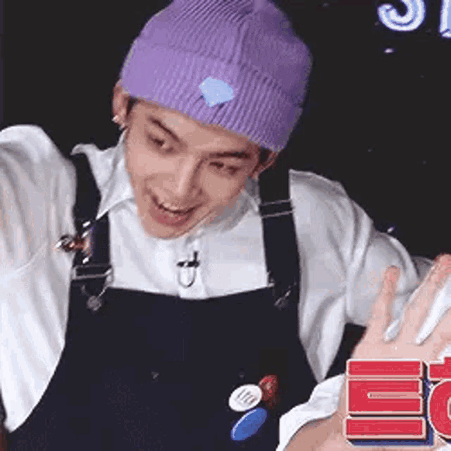 a man wearing a purple beanie and overalls is giving a peace sign .
